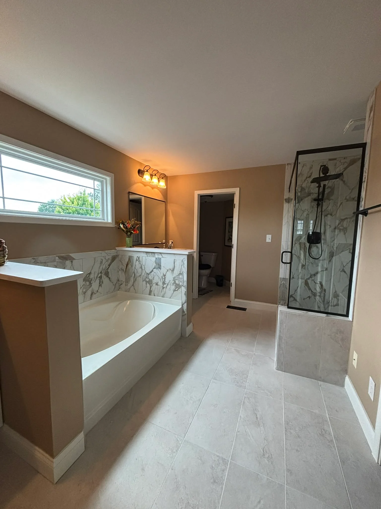 Master bathroom with marble tile tub surround, frameless walk-in shower, and large-format tile flooring in Carmel, IN