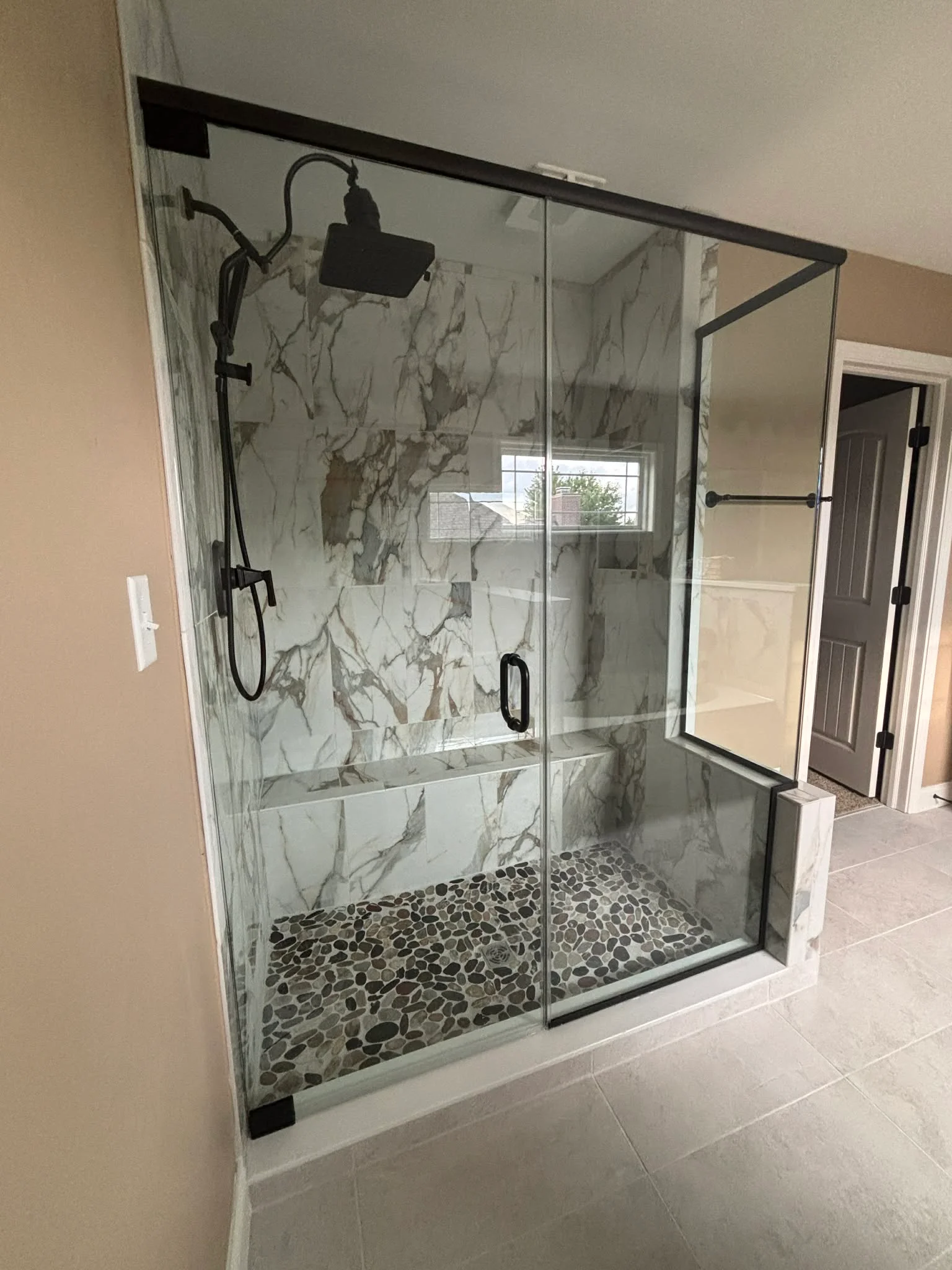 Spa-style walk-in shower with marble-look porcelain tile, river rock floor, and frameless glass enclosure in Indianapolis, IN