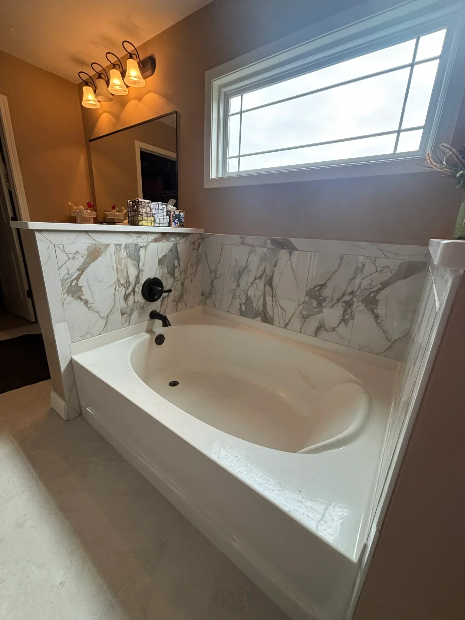 Freestanding soaking tub with marble tile surround and black fixtures in renovated master bathroom in Fishers, IN